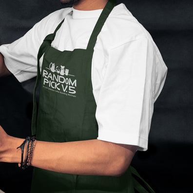 Side view of a barista wearing a dark green apron leaning against a metal shelf in a moody cafe environment, ideal for staff uniform branding mockup