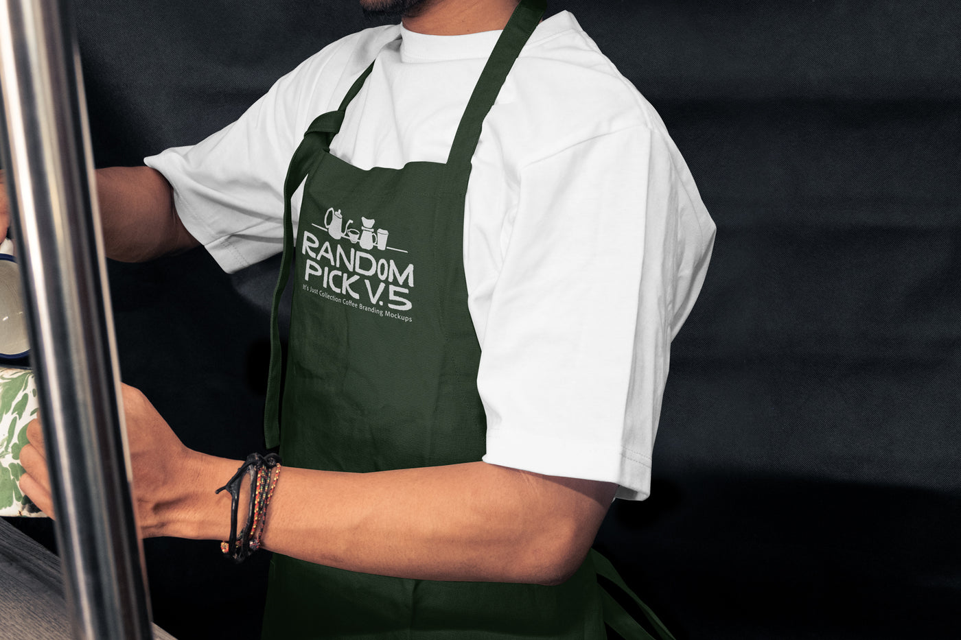 Side view of a barista wearing a dark green apron leaning against a metal shelf in a moody cafe environment, ideal for staff uniform branding mockup