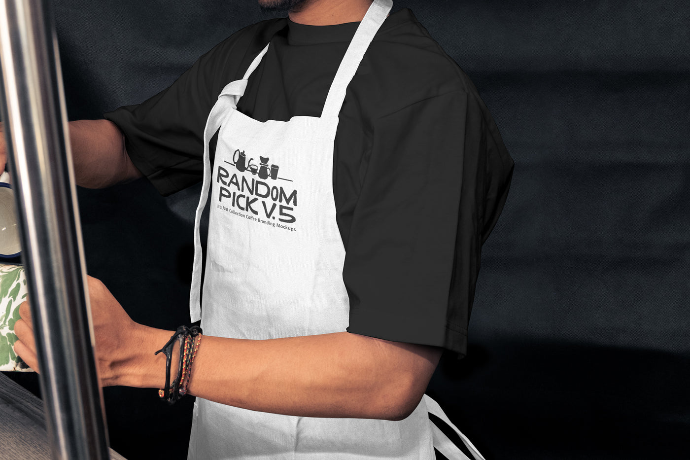 Side view of a barista wearing a white apron leaning against a metal shelf in a moody cafe environment, ideal for staff uniform branding mockup