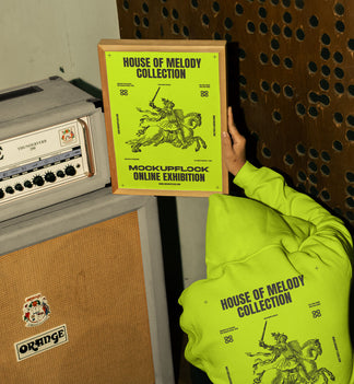This high quality poster mockup features a person wearing a hoodie holding a poster frame in front of an amplifier in a music studio. This aesthetic print mockup was created for Adobe Photoshop.