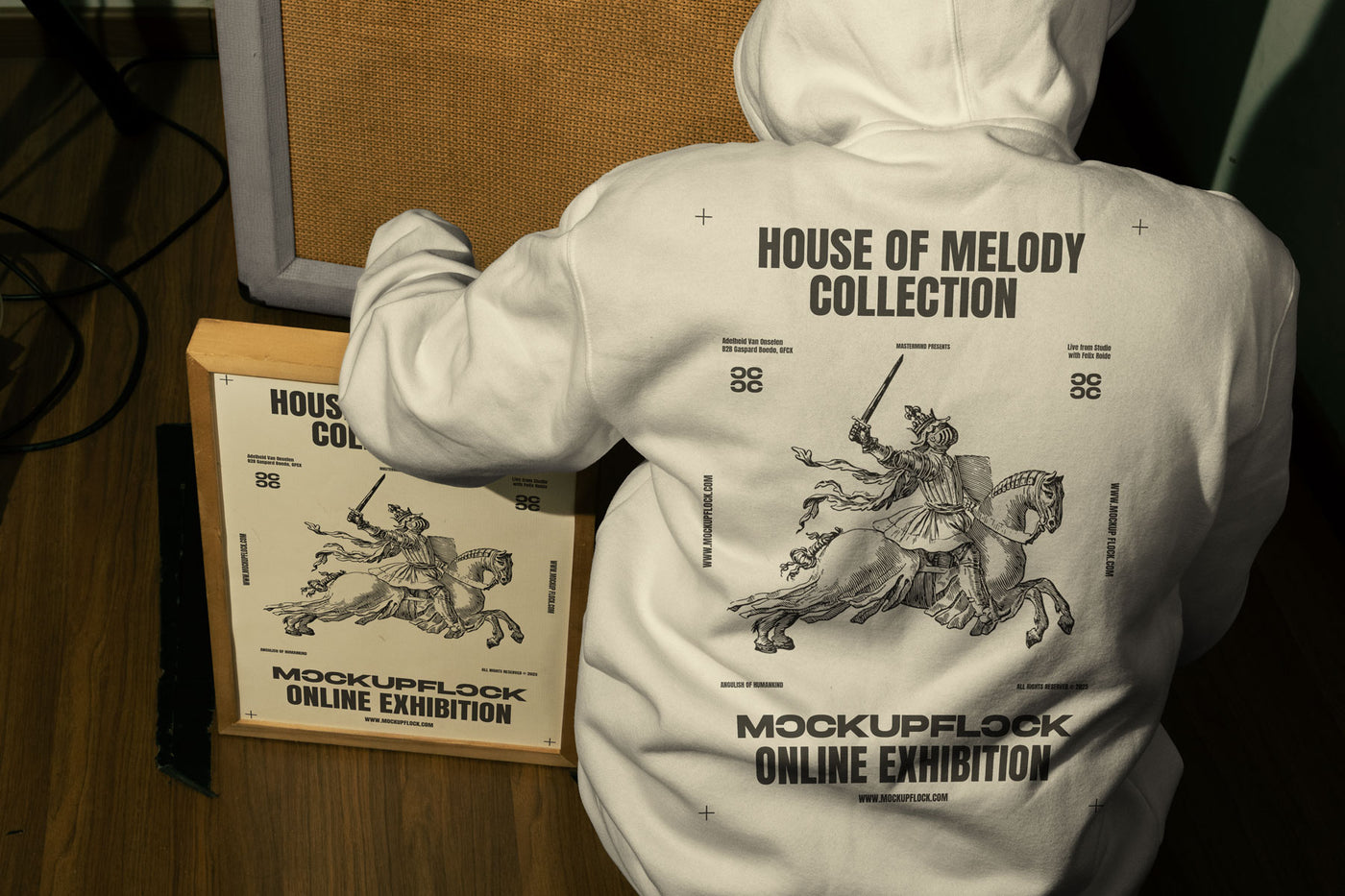 This high quality poster mockup features a person wearing a hoodie sitting next to a poster frame in a music studio. This aesthetic print mockup was created for Adobe Photoshop.