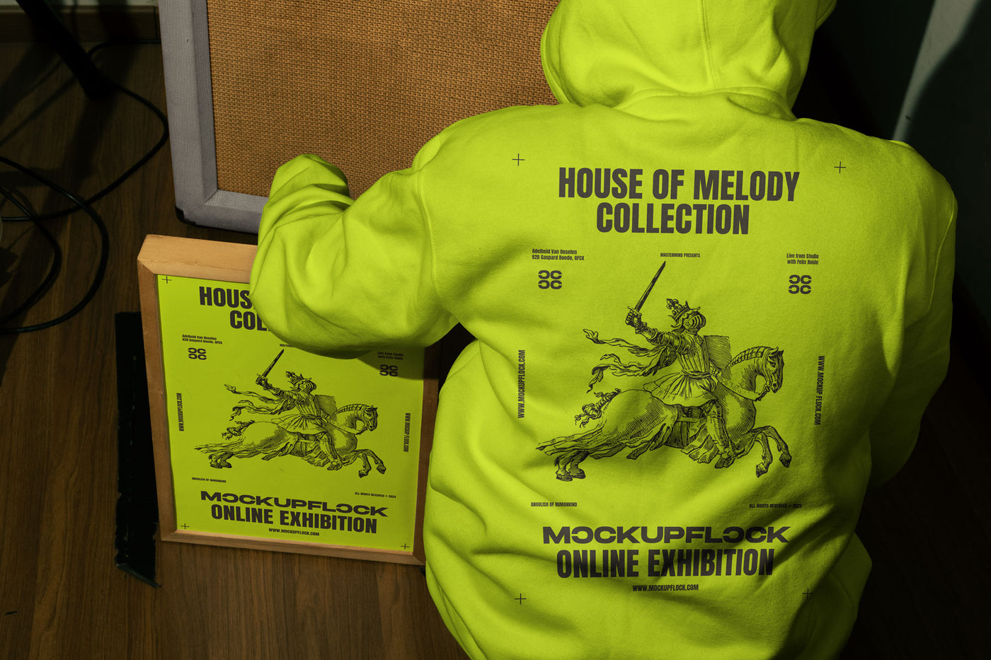 poster frame mockup features a person wearing a hoodie sitting next to a poster frame