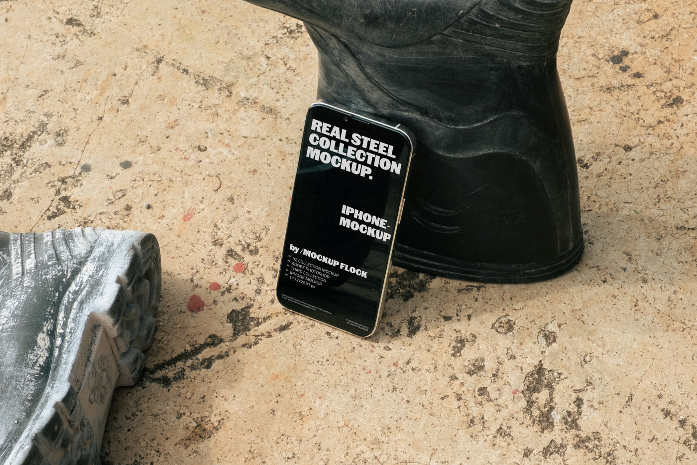 MockupFlock Real Steel Collection iPhone mockup leaning against a black rubber boot on a rough, dusty concrete floor, showcasing realistic lighting and industrial textures.