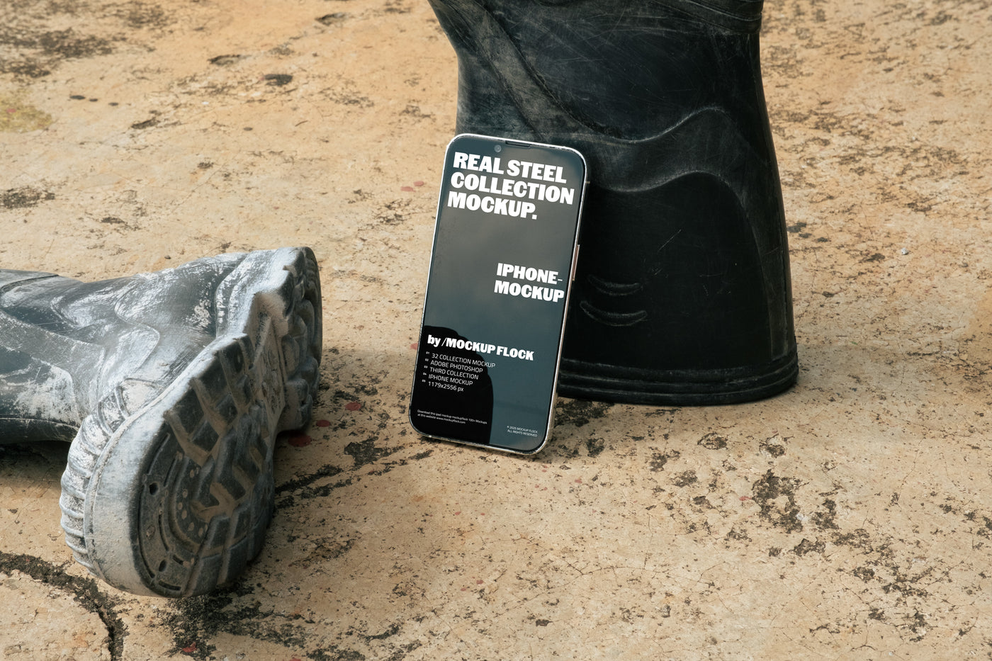 MockupFlock Real Steel Collection iPhone mockup leaning against a black rubber boot on a rough, dusty concrete floor, showcasing realistic lighting and industrial textures.
