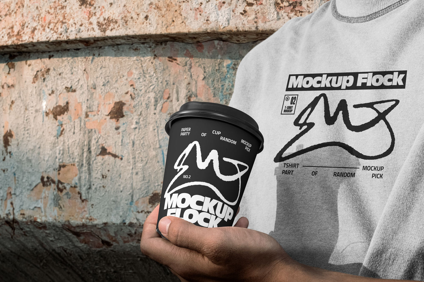 Person wearing a white t-shirt holding a black paper coffee cup with custom branding against an urban textured wall