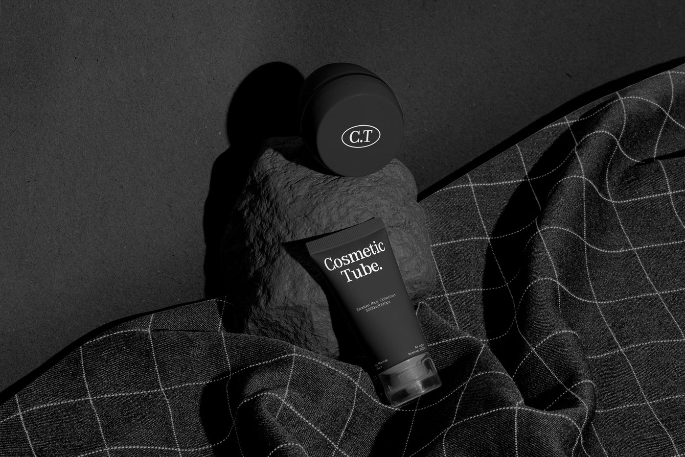 A cosmetic product arrangement featuring a black jar mockup and a black tube mockup labeled 'Cosmetic Tube.' resting on a dark stone against a dark background with draped dark fabric.
