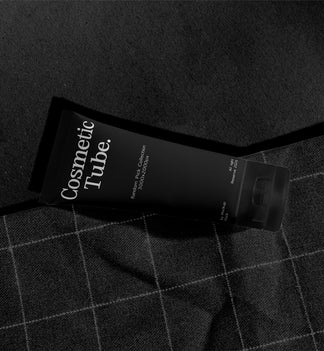 Cosmetic black tube mockup lying diagonally on orange fabric with checkered stitch pattern