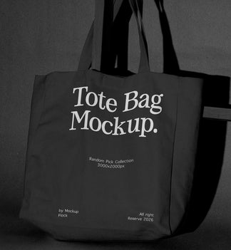 A dark tote bag with large white text reading 'Tote Bag Mockup.' hanging against a dark gray wall, with smaller mockup text below.