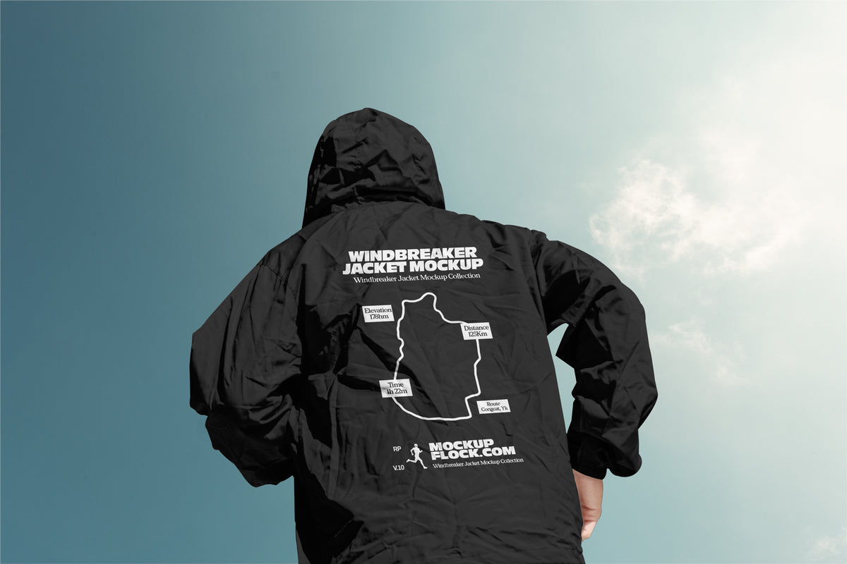 A person viewed from behind wearing a black hooded windbreaker jacket with a large white mockup graphic and text printed on the back, set against a blue sky with light clouds.