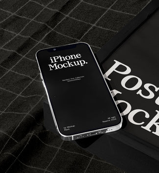 A smartphone mockup with a black screen displaying 'iPhone Mockup.' lies on a dark plaid fabric surface next to a black poster mockup cover with large white text.