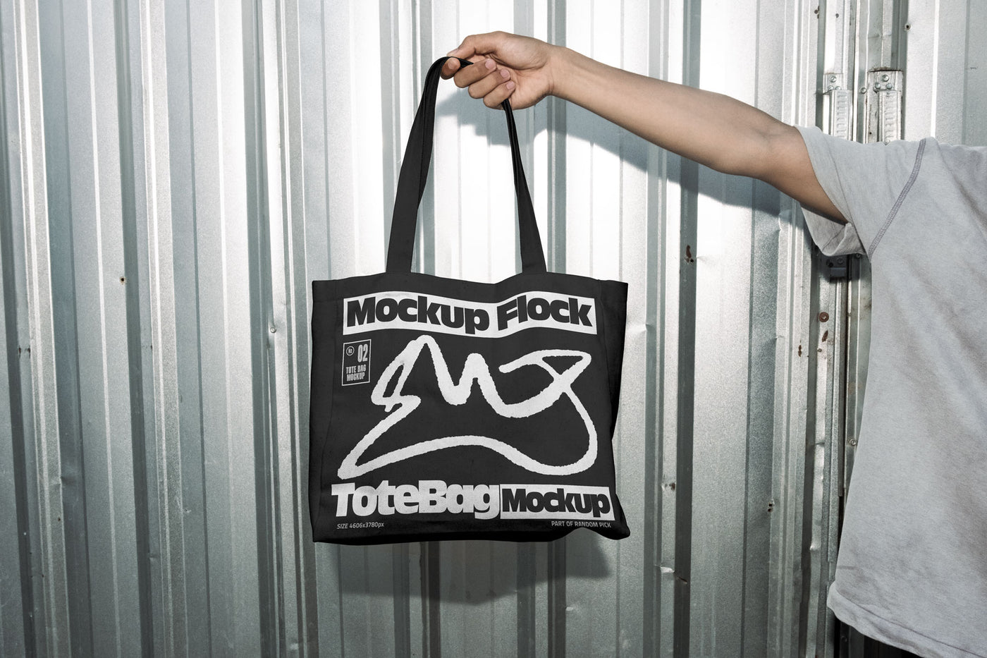 Hand holding a black tote bag featuring an urban graphic design against a silver corrugated metal wall