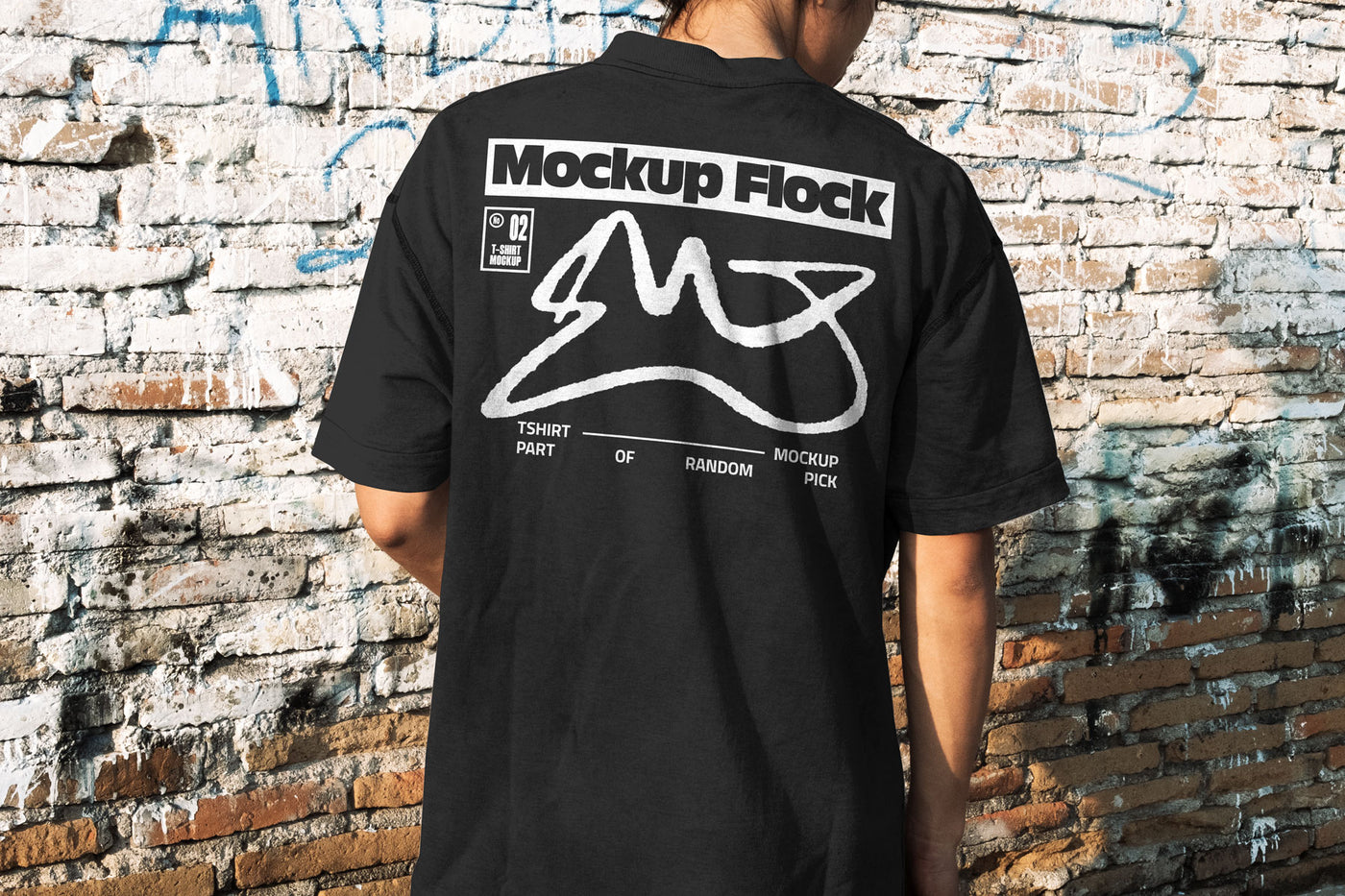 Back view of a person wearing a black streetwear t-shirt with custom graphic design, standing against a distressed brick wall