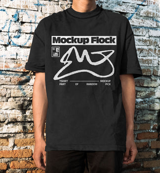 Front view of a man wearing a black streetwear t-shirt with graphic design, posed in front of an aged, textured brick wall