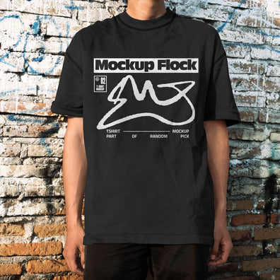 Front view of a man wearing a black streetwear t-shirt with graphic design, posed in front of an aged, textured brick wall
