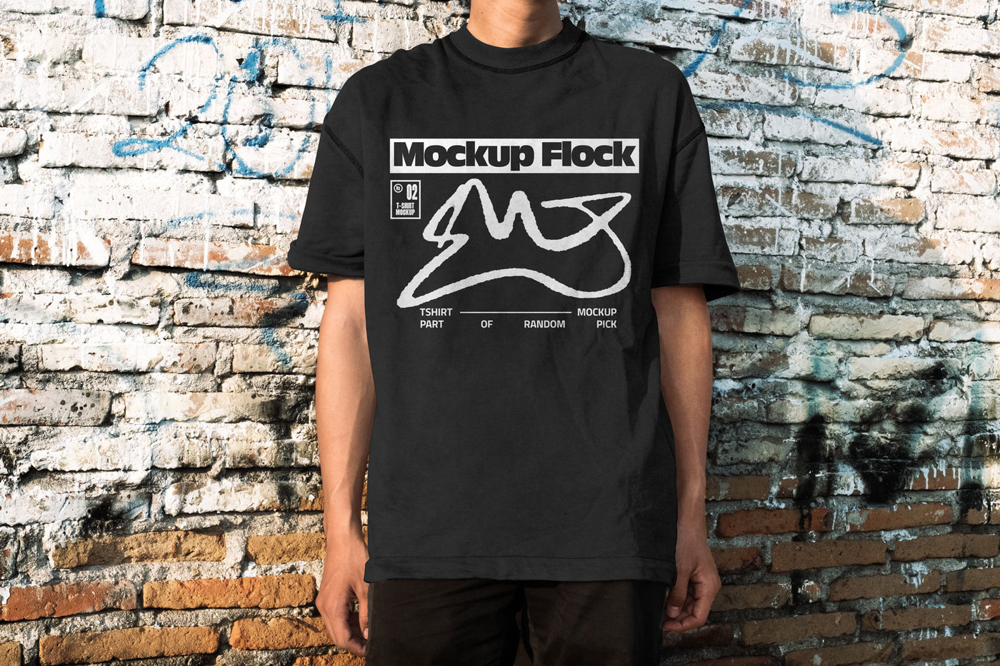 Front view of a man wearing a black streetwear t-shirt with graphic design, posed in front of an aged, textured brick wall