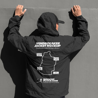 Black hooded windbreaker jacket mockup back view with model's hands raised against grey wall