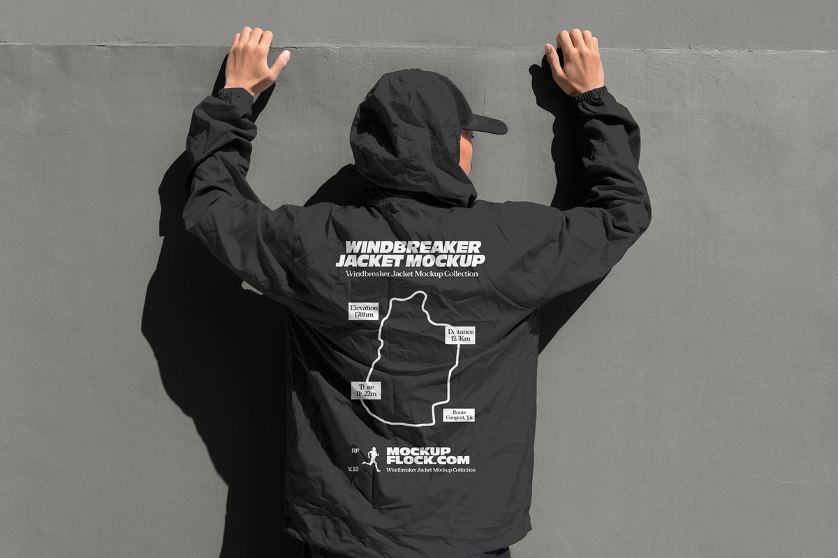Black hooded windbreaker jacket mockup back view with model's hands raised against grey wall