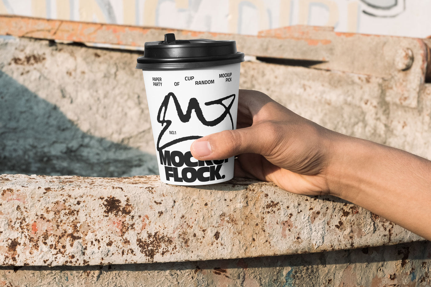 Close-up of a hand holding a white paper coffee cup with a custom logo design against an industrial rusty metal background