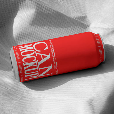 Red beverage can lying on wrinkled white fabric with dramatic shadow, minimal studio mockup