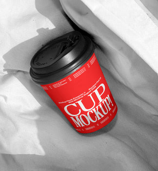 Red paper coffee cup mockup with black lid on wrinkled white fabric, minimal studio mockup