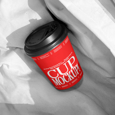 Red paper coffee cup mockup with black lid on wrinkled white fabric, minimal studio mockup