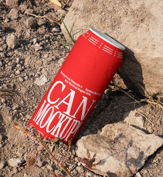 Red beverage can leaning against a rock on dry dirt ground with dried grass, outdoor mockup