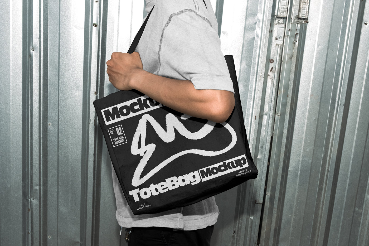 Person carrying a black canvas tote bag over the shoulder with custom graphic print, standing in front of an industrial metal door