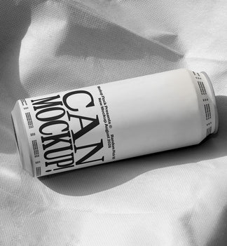 White beverage can lying on wrinkled white fabric with dramatic shadow, minimal studio mockup