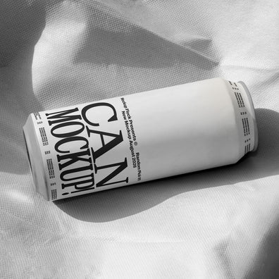 White beverage can lying on wrinkled white fabric with dramatic shadow, minimal studio mockup