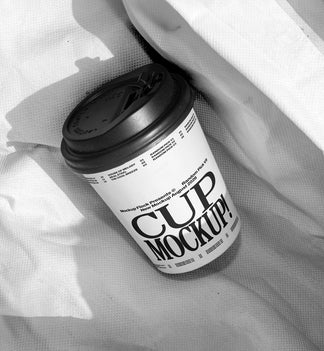 White paper coffee cup mockup with black lid on wrinkled white fabric, minimal studio mockup