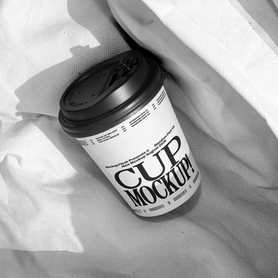 White paper coffee cup mockup with black lid on wrinkled white fabric, minimal studio mockup