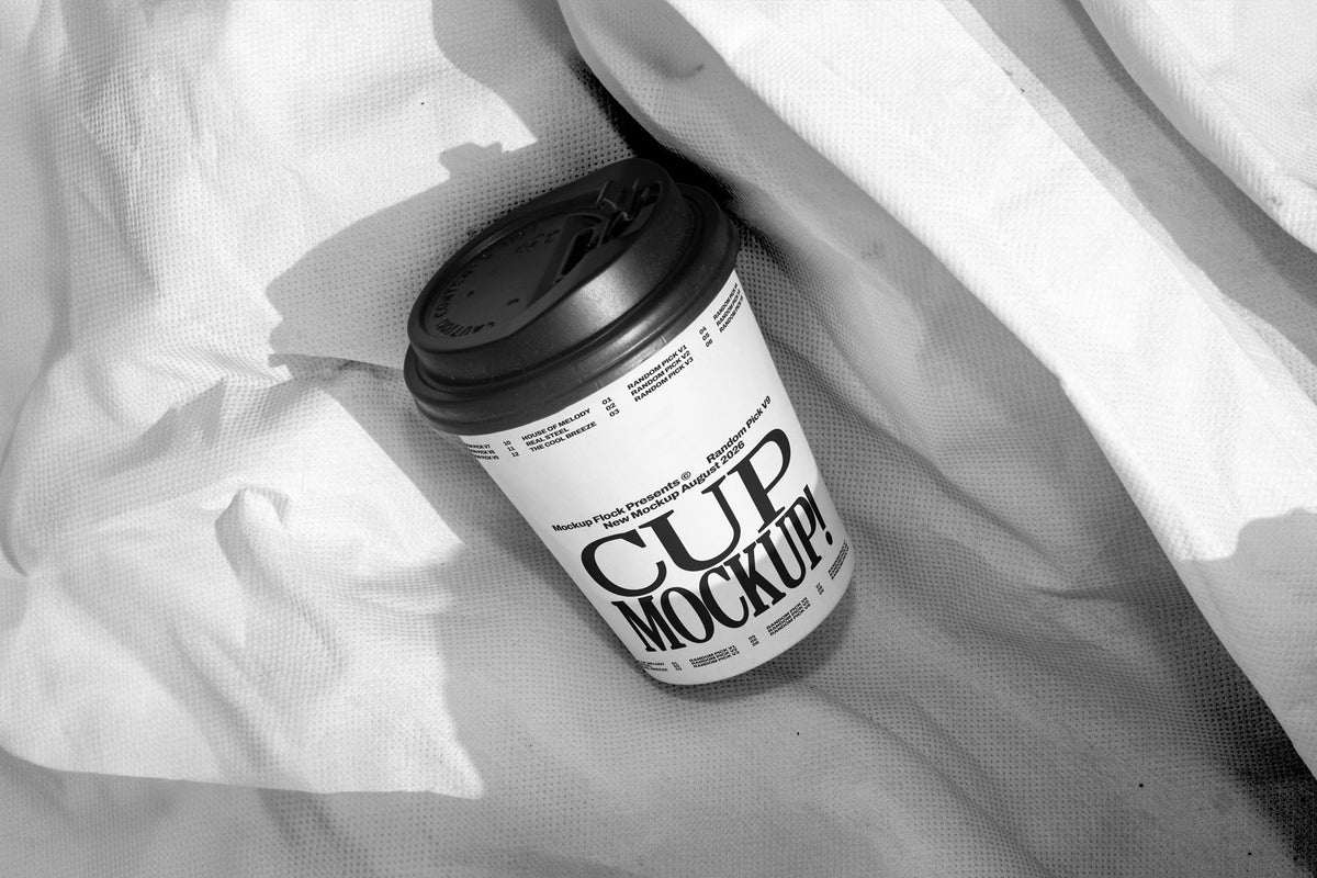 White paper coffee cup mockup with black lid on wrinkled white fabric, minimal studio mockup