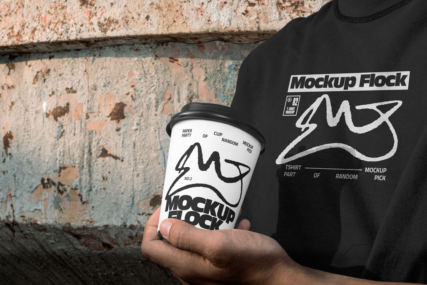 Person wearing a black t-shirt holding a white paper coffee cup with custom branding against an urban textured wall