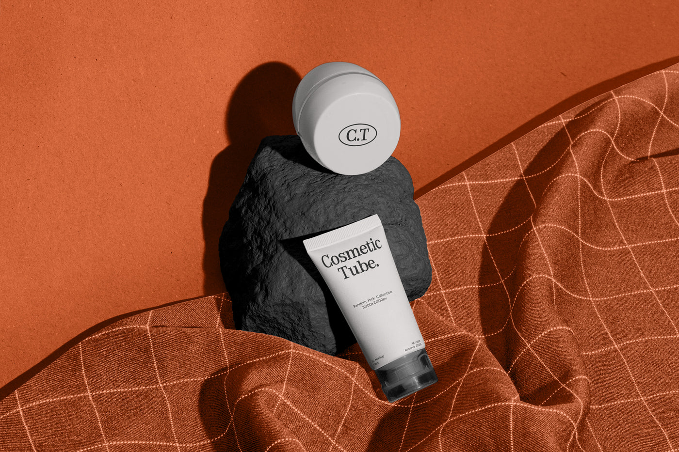 A cosmetic product arrangement featuring a white jar mockup and a white tube mockup labeled 'Cosmetic Tube.' resting on a dark stone against a warm terracotta background with draped orange fabric.