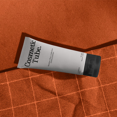 Cosmetic white tube mockup lying diagonally on orange fabric with checkered stitch pattern