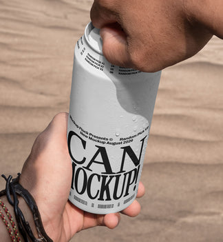 Close-up of hands opening a white beverage can mockup outdoors with desert sand background, lifestyle mockup