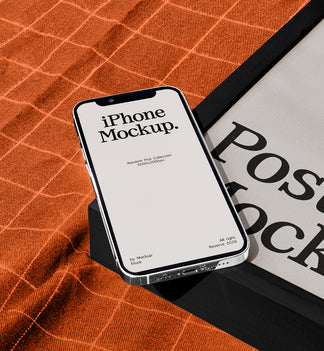 A smartphone mockup displaying 'iPhone Mockup.' on its screen, resting on a black stand over an orange textured fabric next to a black-framed poster with 'Poster Mockup' text.