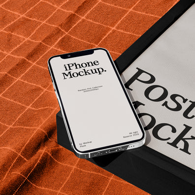 A smartphone mockup displaying 'iPhone Mockup.' on its screen, resting on a black stand over an orange textured fabric next to a black-framed poster with 'Poster Mockup' text.