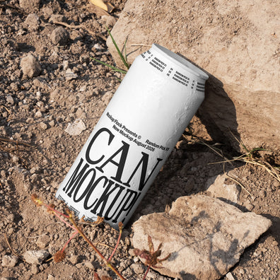 White beverage can leaning against a rock on dry dirt ground with dried grass, outdoor mockup