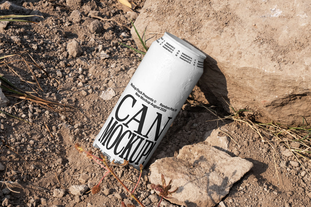 White beverage can leaning against a rock on dry dirt ground with dried grass, outdoor mockup