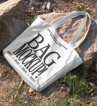 White canvas tote bag mockup with long handles lying on rocks and dirt ground outdoors, mockup