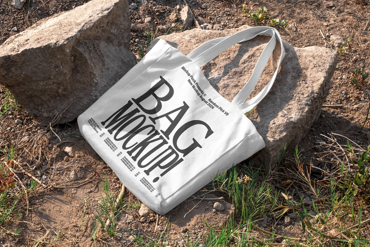 White canvas tote bag mockup with long handles lying on rocks and dirt ground outdoors, mockup