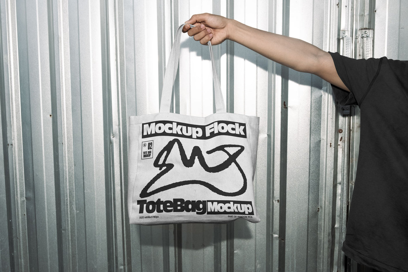 Hand holding a white tote bag featuring an urban graphic design against a silver corrugated metal wall
