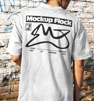 Back view of a person wearing a white streetwear t-shirt with custom graphic design, standing against a distressed brick wall