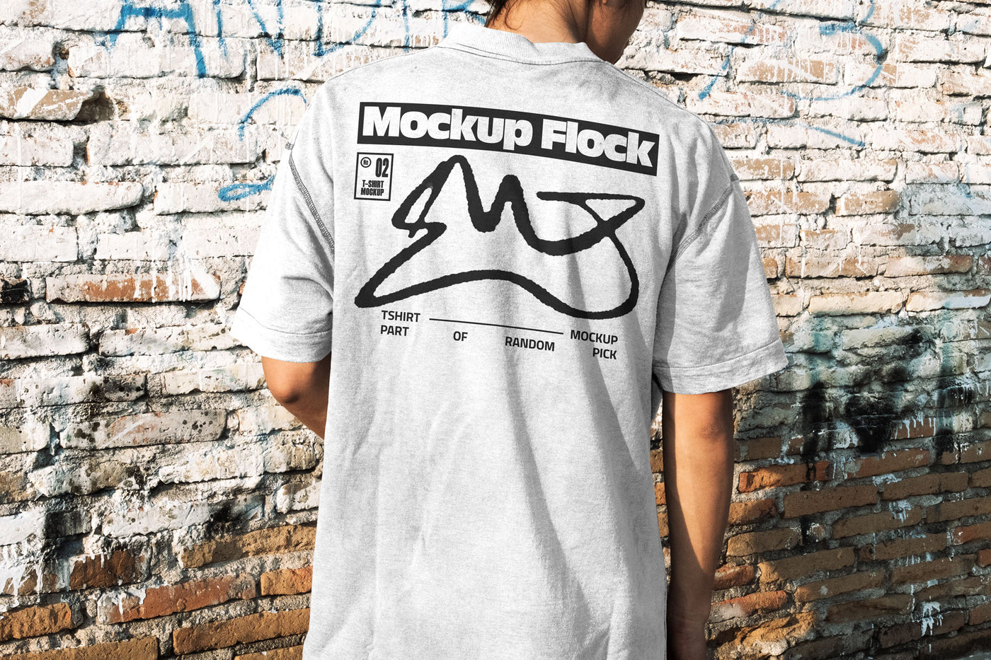 Back view of a person wearing a white streetwear t-shirt with custom graphic design, standing against a distressed brick wall