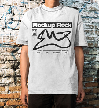 Front view of a man wearing a white streetwear t-shirt with graphic design, posed in front of an aged, textured brick wall