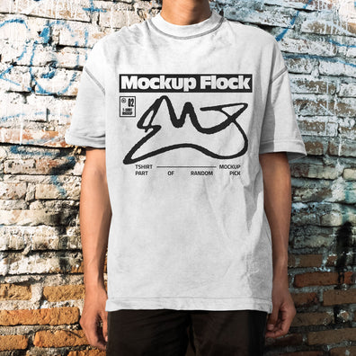 Front view of a man wearing a white streetwear t-shirt with graphic design, posed in front of an aged, textured brick wall