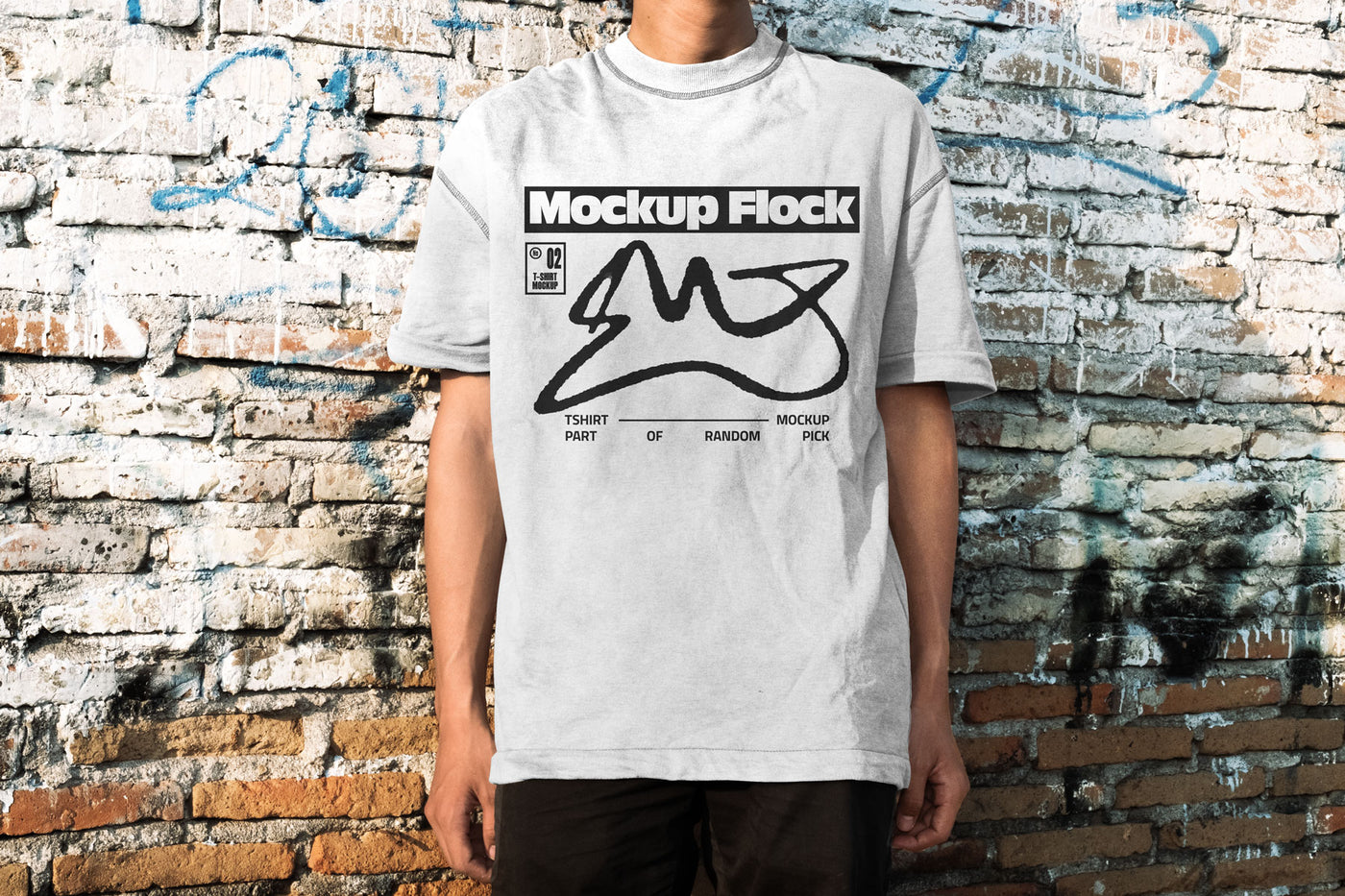 Front view of a man wearing a white streetwear t-shirt with graphic design, posed in front of an aged, textured brick wall