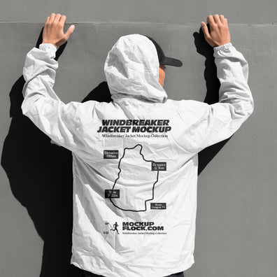 White hooded windbreaker jacket mockup back view with model's hands raised against grey wall