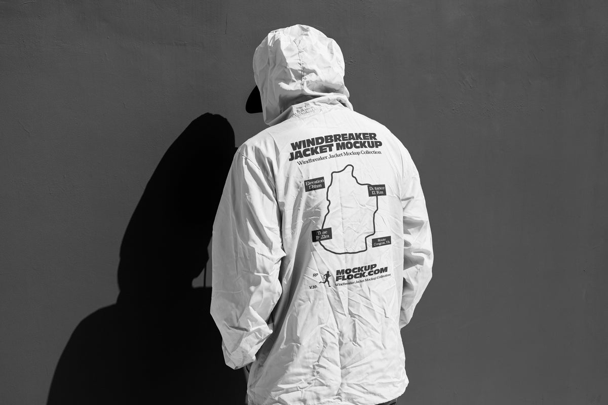 A person shown from behind wearing a white hooded jacket mockup with a large black printed graphic and text on the back, standing against a dark gray wall that casts a strong shadow.